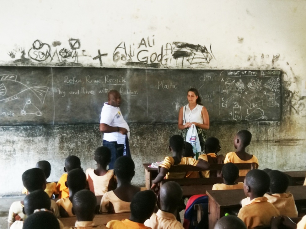 Ein Foto zeigt die kulturweit-Freiwillige mit einem Lehrer vor einer Tafel. Im Bildvordergrund sind einige Schüler*innen zu erkennen.