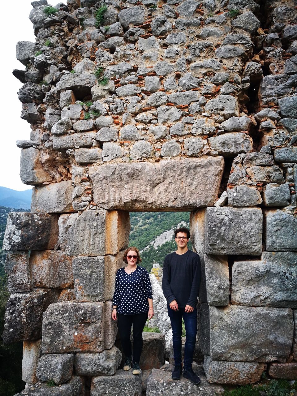 Ein Foto von zwei Menschen vor einer alten Steinmauer.