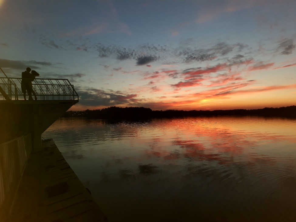 EIn Foto von einem Sonnenaufgang oder -untergang über einem Gewässer.