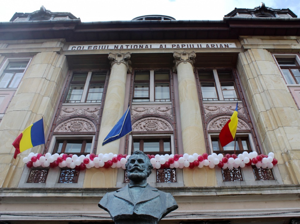 Ein Foto von einem repräsentativen alten Gebäude, das mit Luftballons und Fahnen geschmückt ist und eine große Bronzebüste von einem Mann an der Fassade trägt.