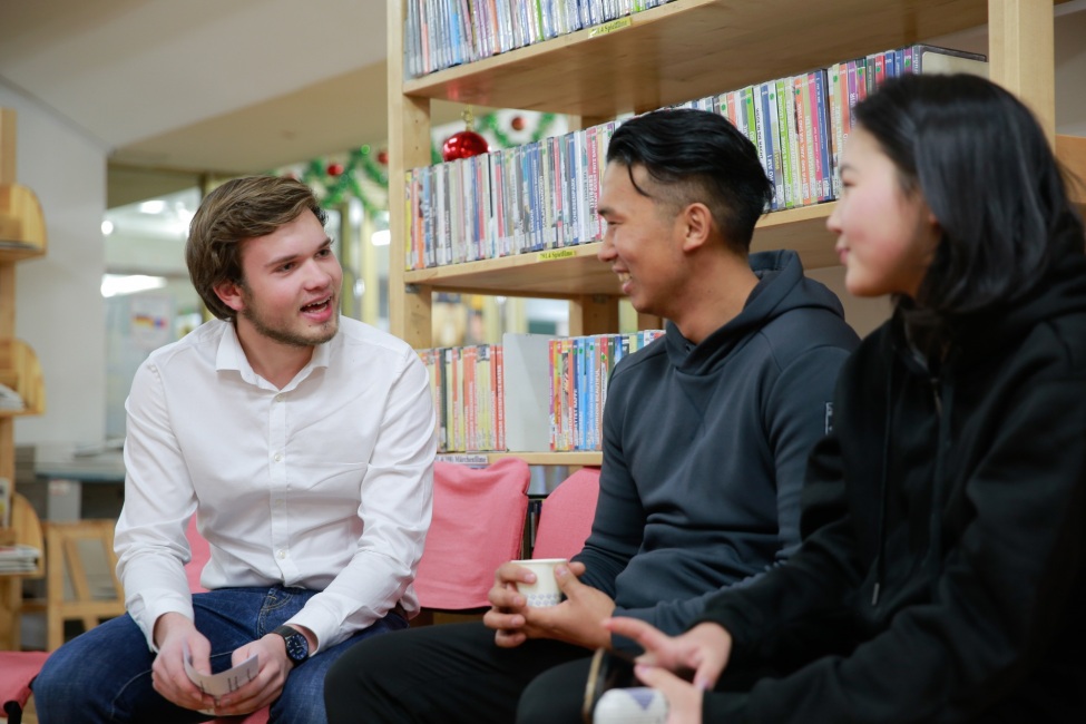 Ein Portraitfoto von dem kulturweit-Freiwilligen mit zwei jungen Menschen vor einem Bücherregal.