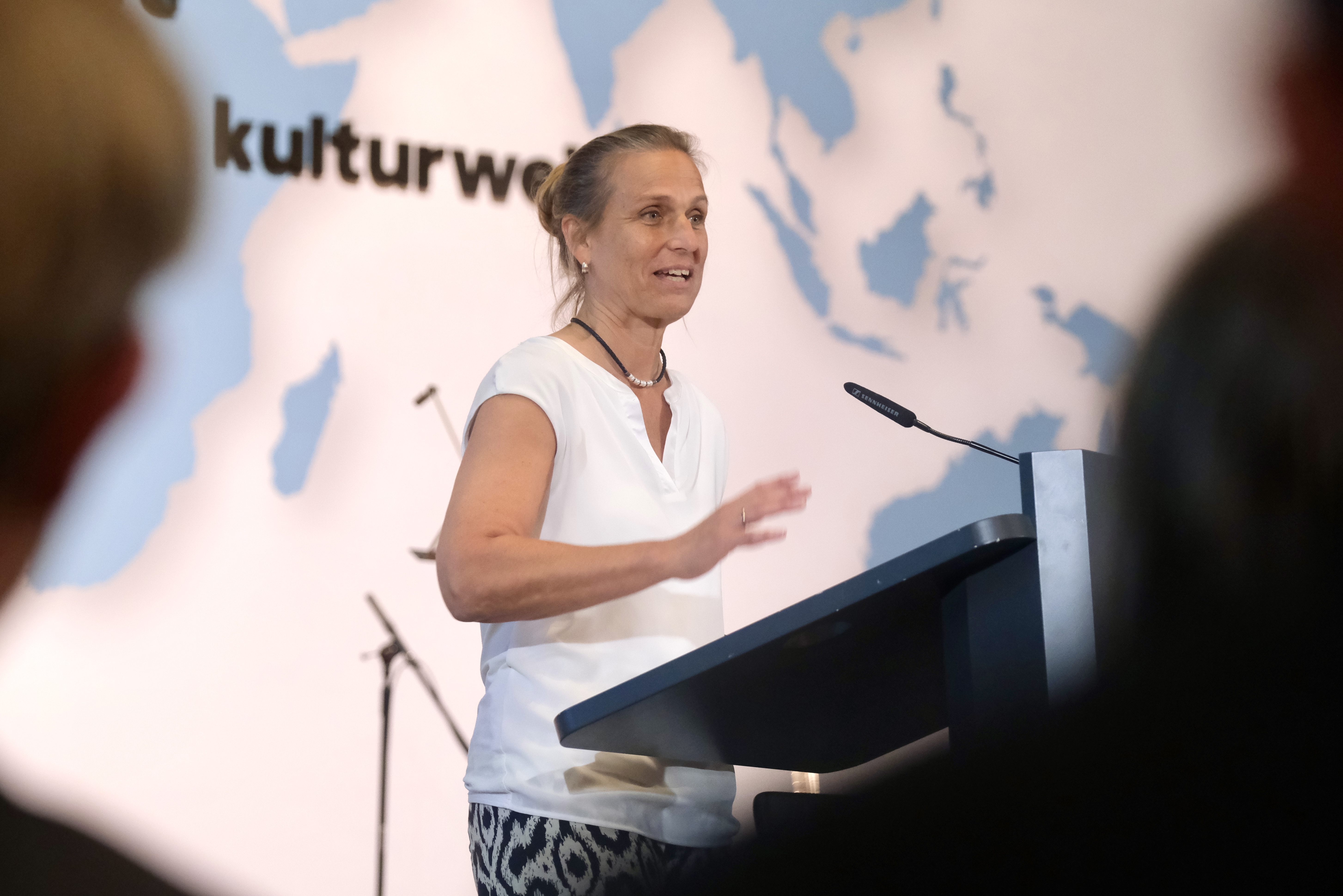 Staatsministerin Katja Keul steht am Rednerpult und spricht vor dem Publikum während des Freiwilligenempfangs im Auswärtigen Amt. Im Hintergrund ist eine Weltkarte mit dem Schriftzug „kulturweit“ zu sehen.