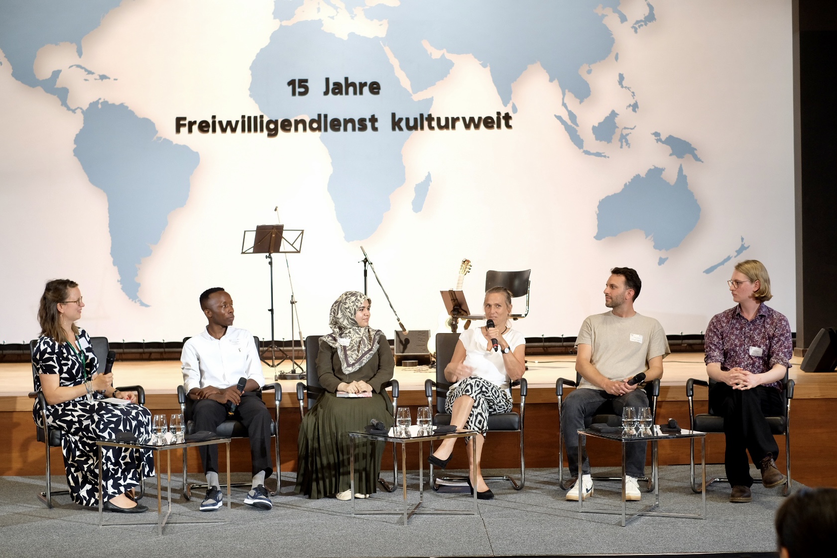 Das Bild zeigt sieben Personen, die auf einem Panel sitzen für den Freiwilligenempfang im Auswärtigen Amt. Darunter befinden sich jeweils zwei ehemalige Incoming- und Outgoing-Teilnehmende sowie Staatsministerin Katja Keul und kulturweit-Leitung Hannah Tümpel.