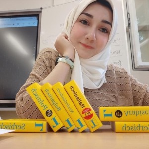 Yomna sitzt lächelnd in einem Klassenraum, vor ihr liegen mehrere Wörterbücher